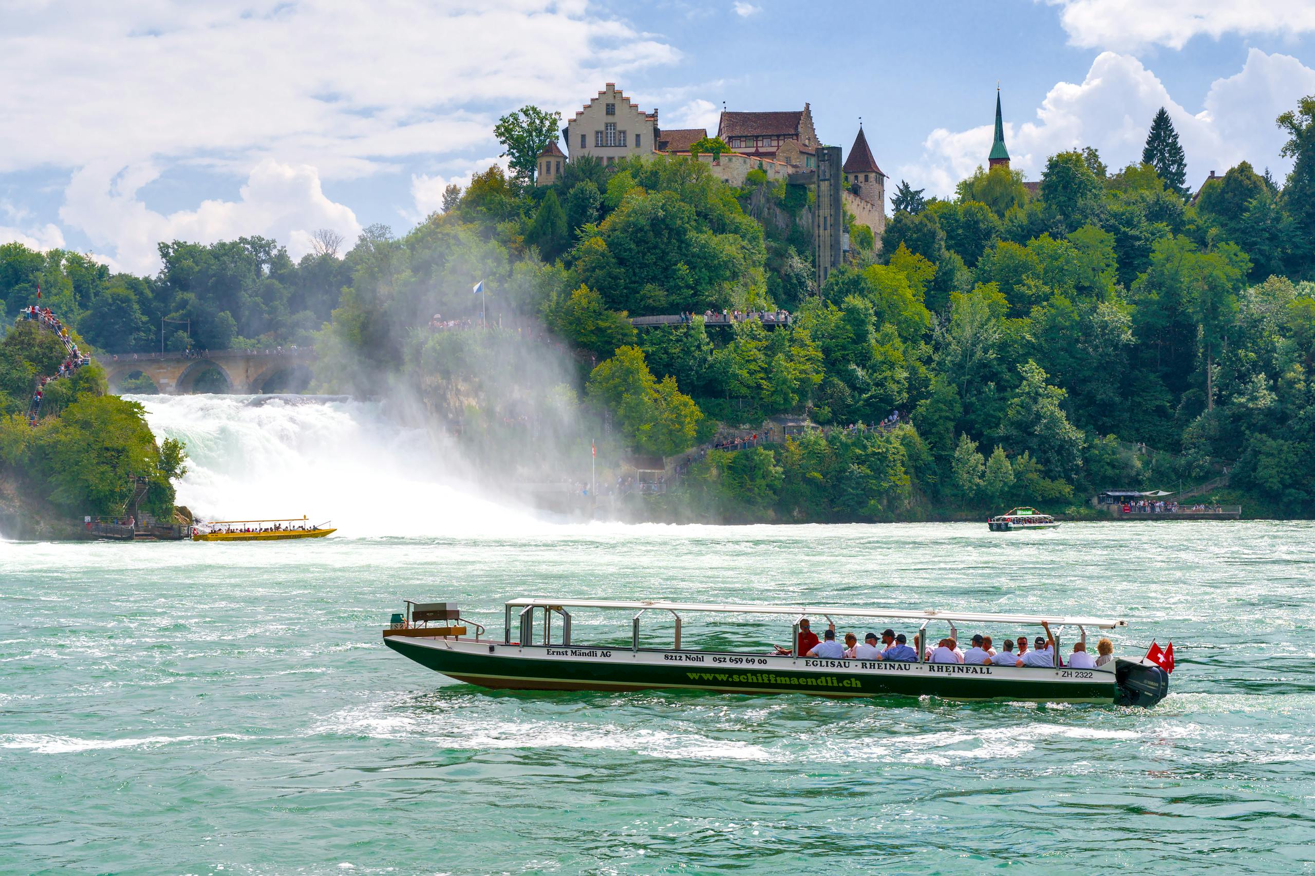 Tourists enjoy a boat ride near the stunning Rhine Falls in Switzerland.
